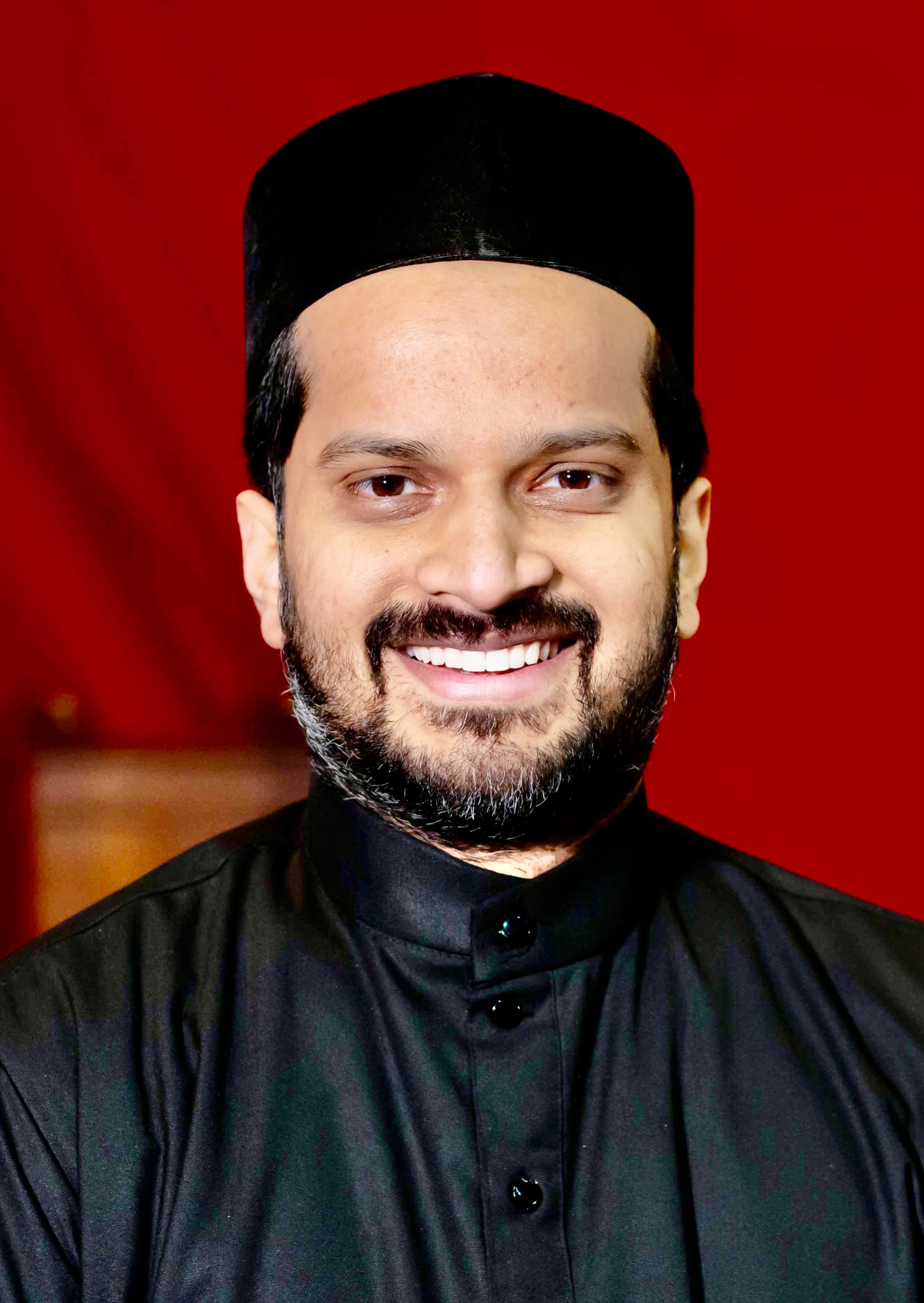 A smiling man in his all black priestly Indian Orthodox garb